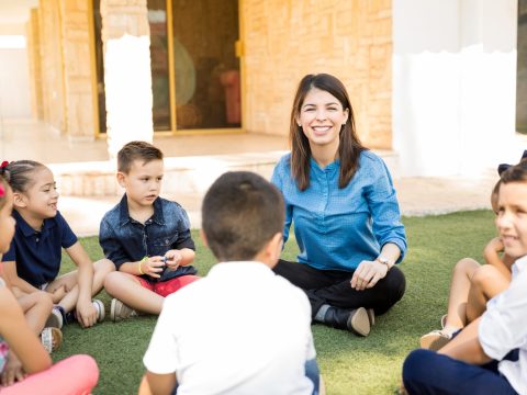 portrait-beautiful-preschool-teacher-having-class-outdoors-with-group-students-smiling